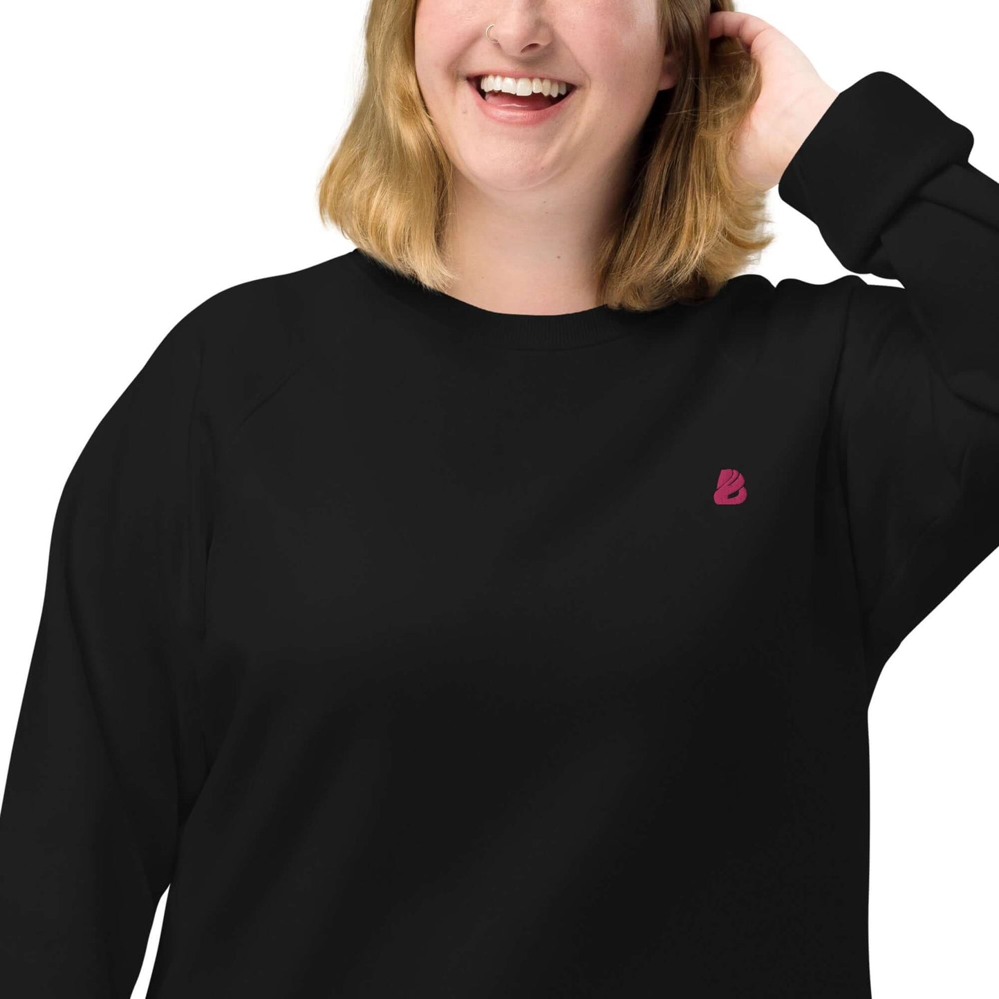 Person wearing Unisex Bio-Raglan-Pullover N°2 in black with a pink emblem, showing soft fleece interior and stylish design.