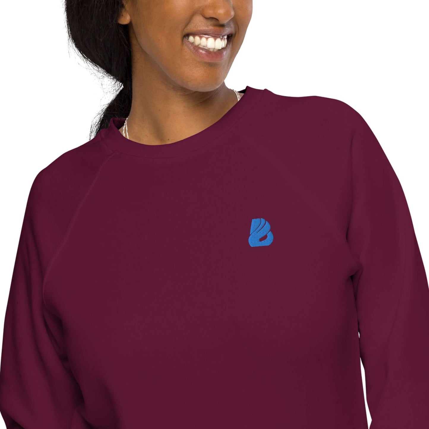 Woman wearing Unisex Bio-Raglan-Pullover N°1 in burgundy with blue logo, showcasing stylish comfort and organic cotton material.