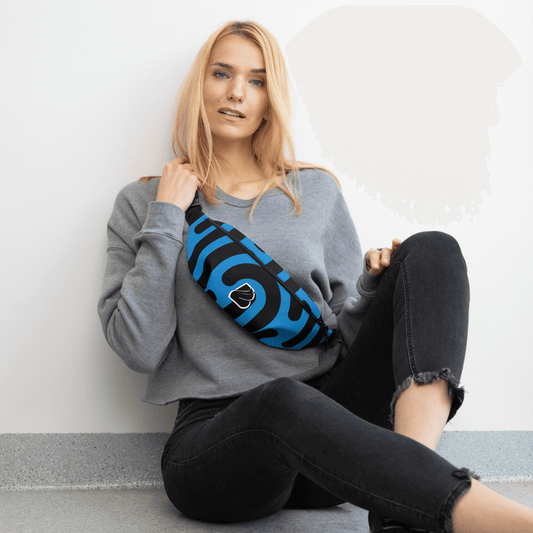 Young woman in a gray sweatshirt and black jeans sitting with a stylish blue striped fanny pack.