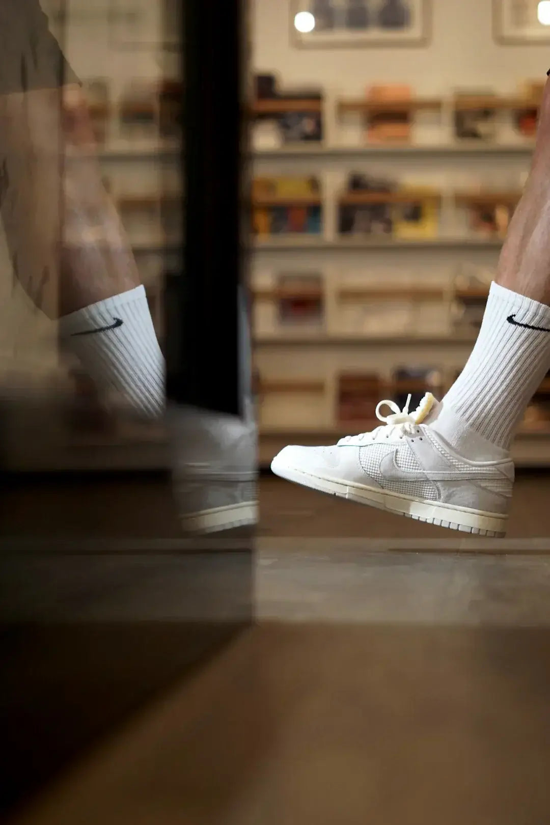 Close-up of a person wearing white Nike sneakers and socks, reflecting in a shop mirror.