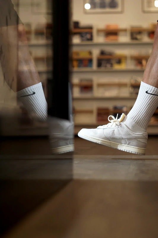 Close-up of a person wearing white Nike sneakers and socks, reflecting in a shop mirror.
