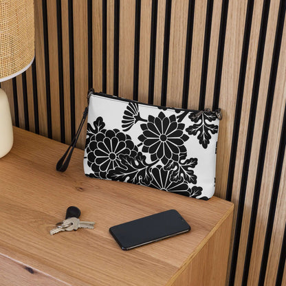 Black and white floral patterned clutch on wooden desk next to keys and smartphone.