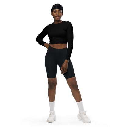 Model wearing Recyceltes Langarm Crop Top mit Allover-Druck N°3, paired with black shorts and white sneakers, posing confidently.