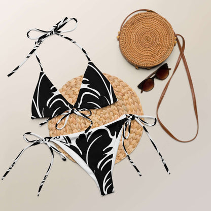 Recycelter Schnürbikini mit Allover-Druck N°0 neben Strohtasche und Sonnenbrille auf neutralem Hintergrund.