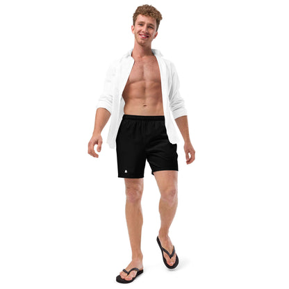 Man wearing Herren-Badehosen N°11 black swim trunks with white shirt and flip-flops, ideal for summer activities.