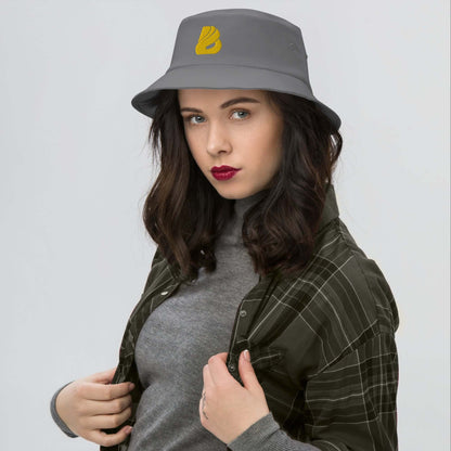 Woman wearing Old School-Fischerhut N°2, a vintage gray bucket hat ideal for fishing, hiking, with yellow logo and stylish design.