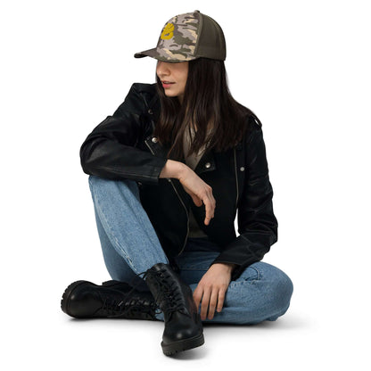 Fashionable woman wearing Trucker-Hat im Camouflage-Look N°0, sitting in a leather jacket and jeans, perfect for outdoor adventures.