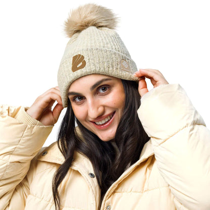Woman wearing Columbia Bommelmütze with pom-pom, beige jacket, and happy expression