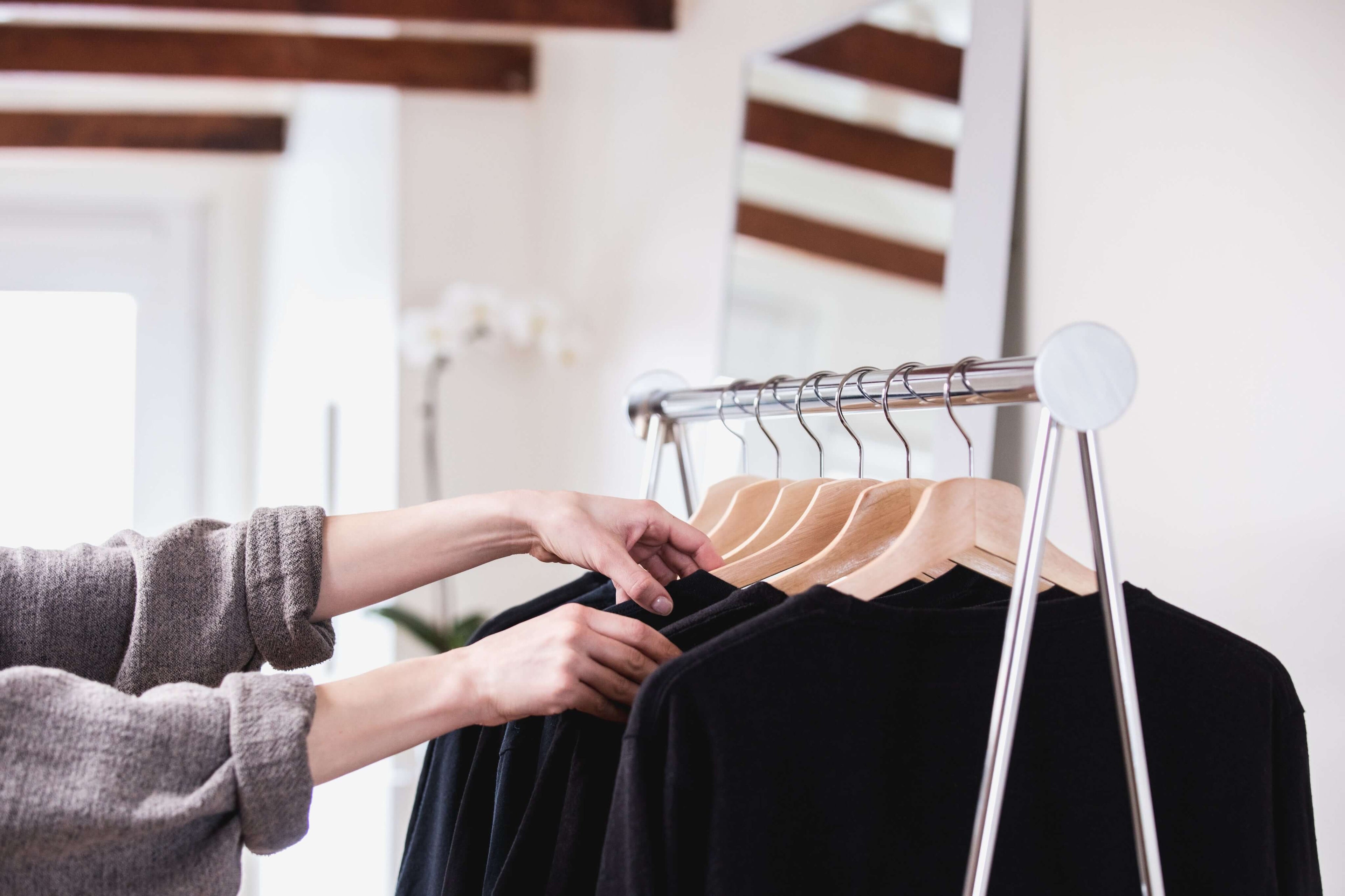 A person adjusting black clothing on hangers in a modern wardrobe setting.