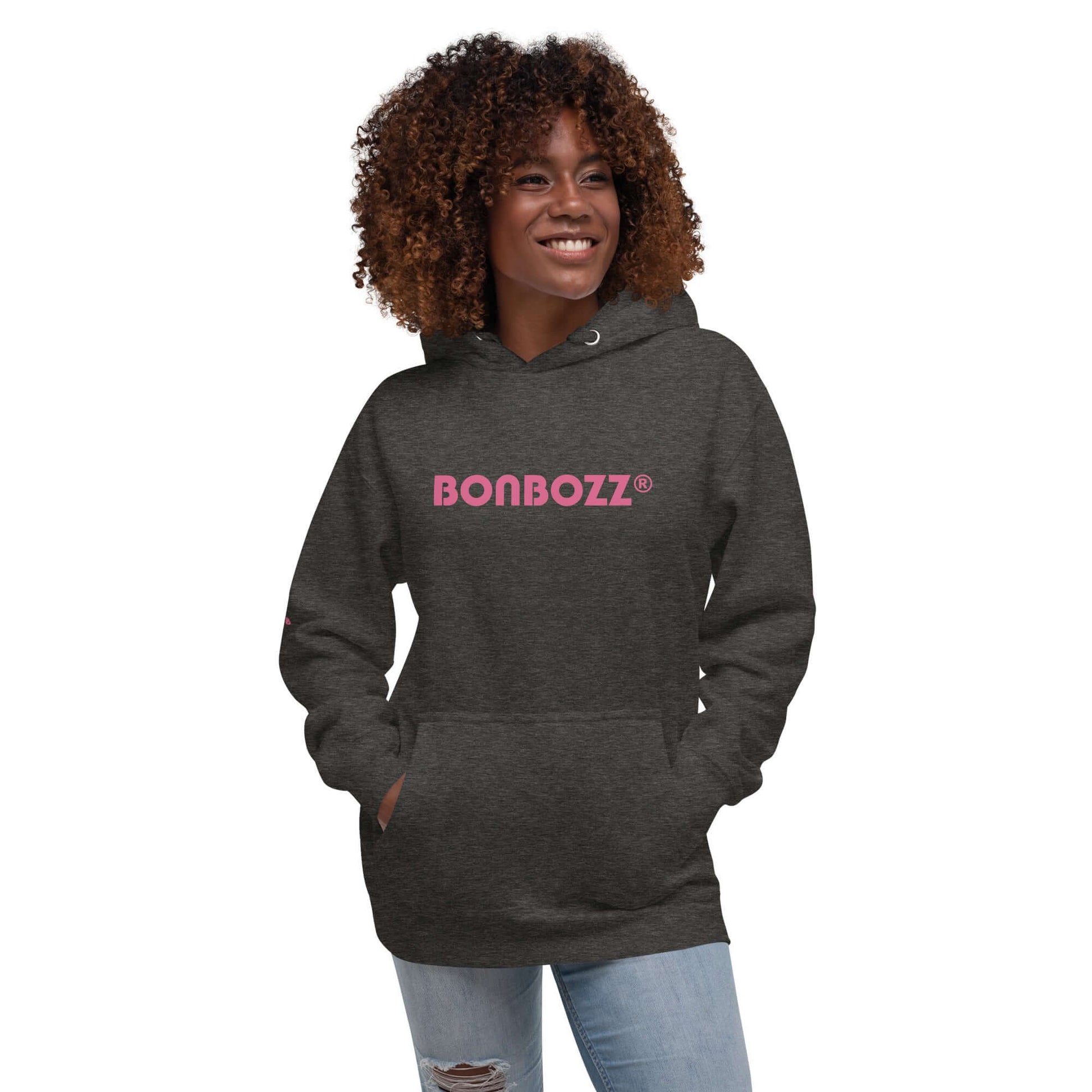 Smiling person wearing a dark gray Unisex-Kapuzenpullover with pink text print and front pocket.