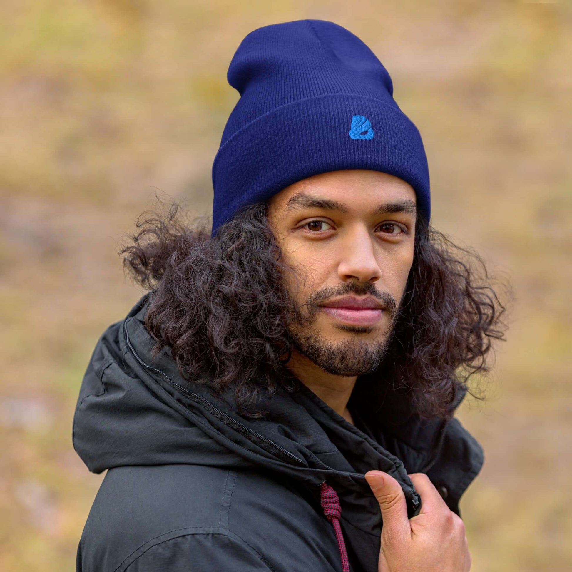 Person wearing a blue Umgeschlagene Beanie with logo, cozy and warm design, fits snugly, unisex style, ideal for chilly weather.