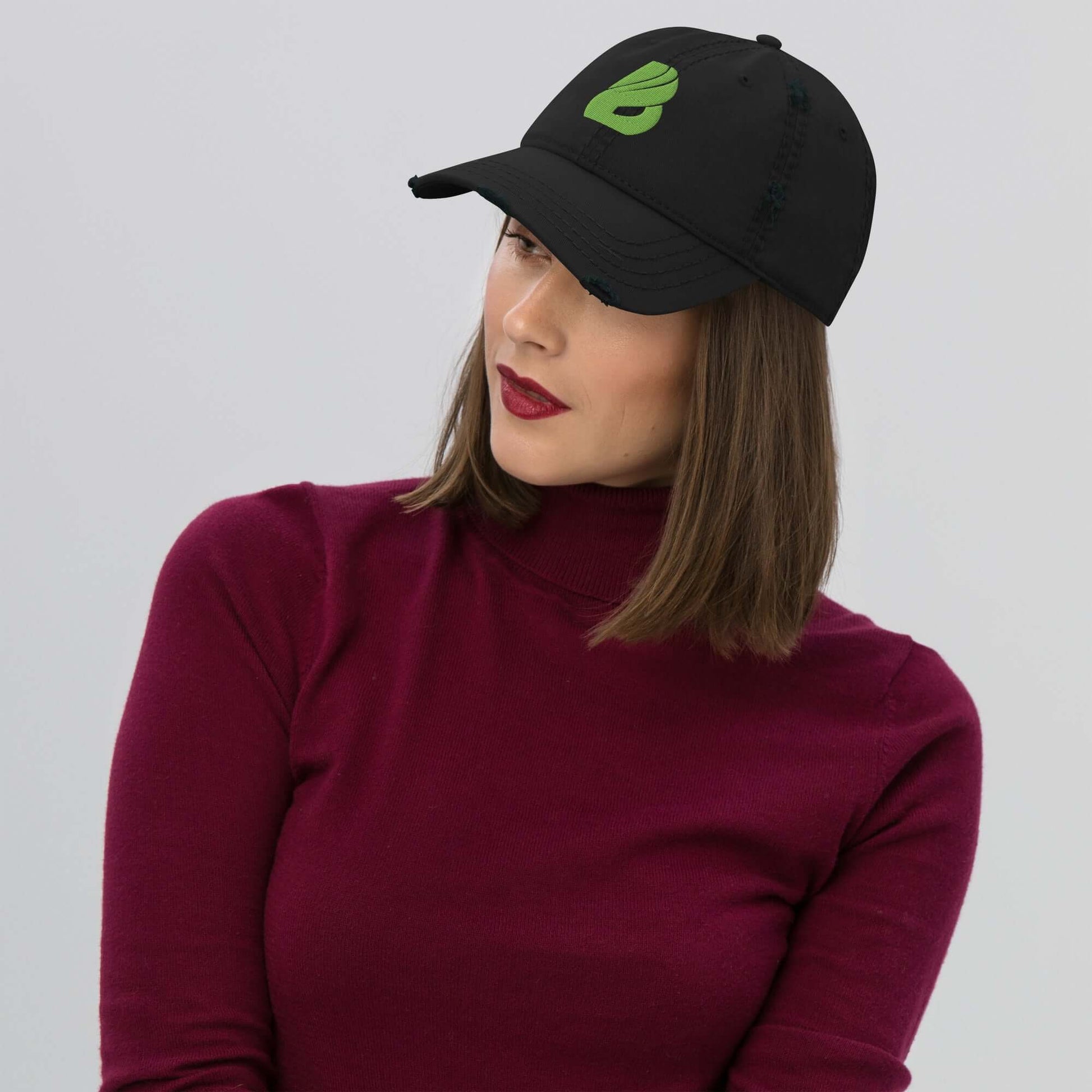 Frau trägt schwarzen Dad-Hat im Used-Look mit Logo, kombiniert mit bordeauxfarbenem Pullover.