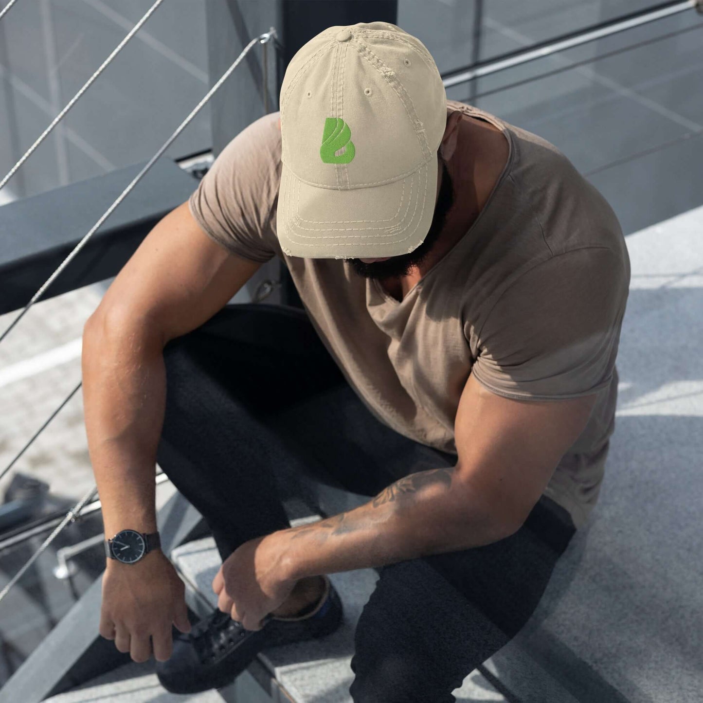 Mann trägt Dad-Hat im Used-Look mit beigem Cap und grünen Logo, ideal für lässige Outfits mit Jeans und T-Shirt auf einer Treppe sitzend.