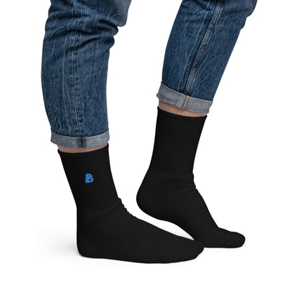 Person wearing black Bestickte Socken N°1 with blue logo, made of 80% cotton, featuring a cushioned sole, manufactured in the USA.