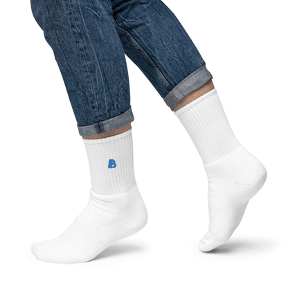 Person wearing Bestickte Socken N°1 with blue logo, showcasing style and comfort; white socks with padded sole and USA-made quality.
