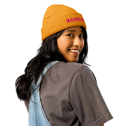 Woman wearing Fischer Beanie N°0 in mustard color, showing the back view with denim overalls and a gray shirt.