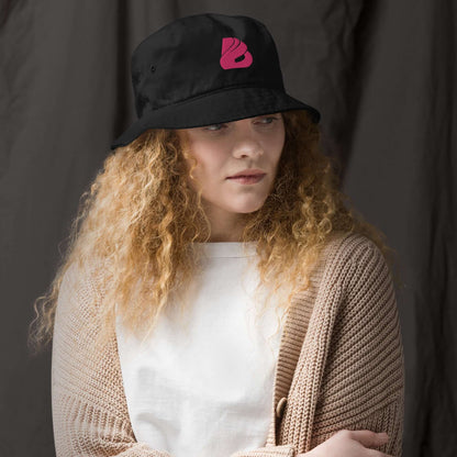 Model wearing Fischerhut aus Bio-Baumwoll-Twill N°1, showcasing stylish and eco-friendly design, black hat with pink logo.