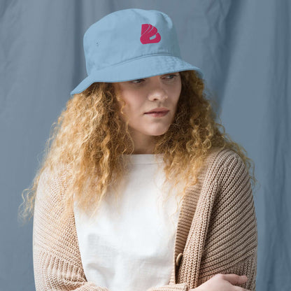 Woman wearing Fischerhut aus Bio-Baumwoll-Twill N°0 with blue color and red logo, highlighting eco-friendly cotton material and simple style.