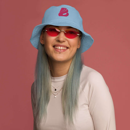Person wearing Fischerhut aus Bio-Baumwoll-Twill N°0 with pink glasses, smiling against a pink background.