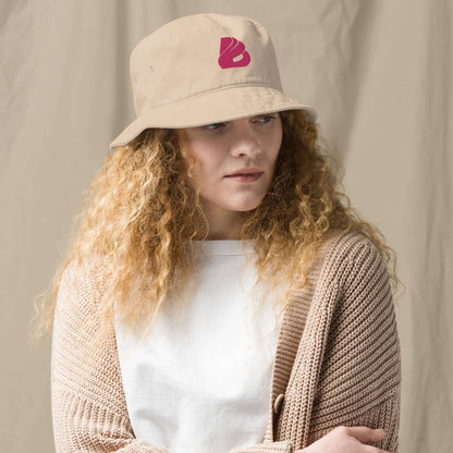 Stylish woman wearing Fischerhut aus Bio-Baumwoll-Twill N°1, a beige organic cotton twill bucket hat with red logo.