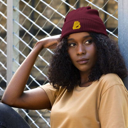 Woman wearing Gerippte Bio-Beanie N°1, a stylish ribbed organic cotton cap, sitting against a metal fence.