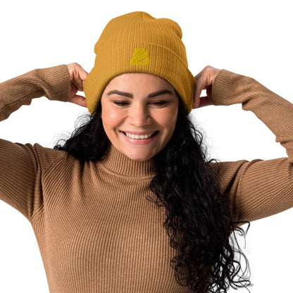 Woman wearing Gerippte Bio-Beanie N°1 made from 100% organic cotton with ribbed cuff in mustard color, smiling and adjusting the beanie.