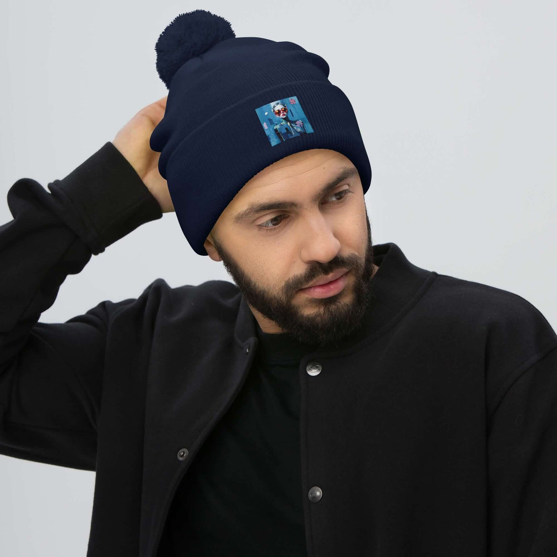 Man wearing a navy blue Bommelmütze with pompom and embroidered patch, black jacket, perfect for cold weather fashion and comfort.