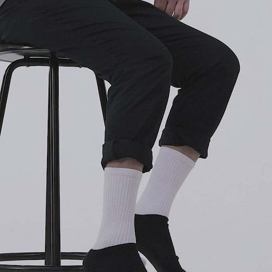 Person wearing Socken N°0, comfortable black-footed socks with ribbed legs, sitting on stool, showcasing vibrant colors and cushioned sole.