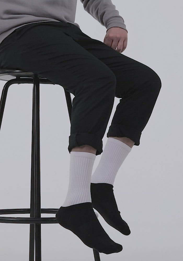 Person wearing Socken N°0, comfortable black-footed socks with ribbed legs, sitting on stool, showcasing vibrant colors and cushioned sole.