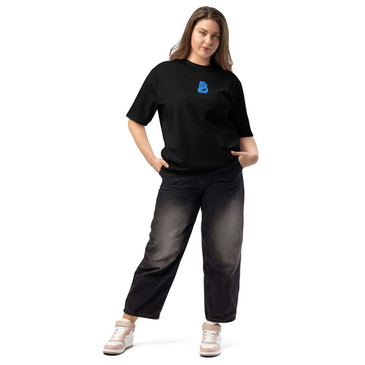 Frau in schwarzem oversized T-Shirt mit blauem Logo, kombiniert mit lässigen Jeans und Sneakers.