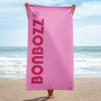Person holding a pink Handtuch with large BONBOZZ logo on the beach