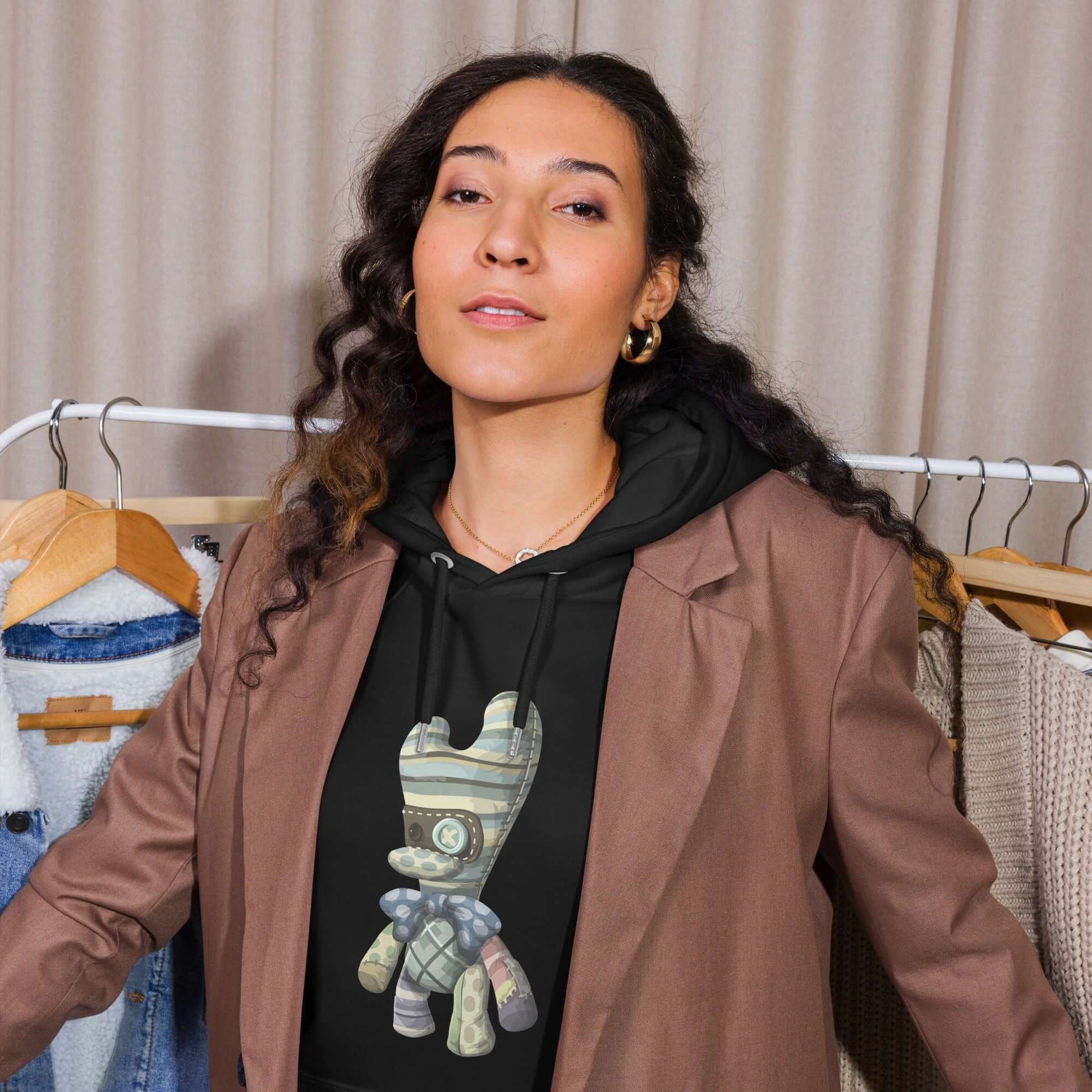 Person wearing Unisex Bio-Raglan-Hoodie with a brown blazer, standing near clothes rack.