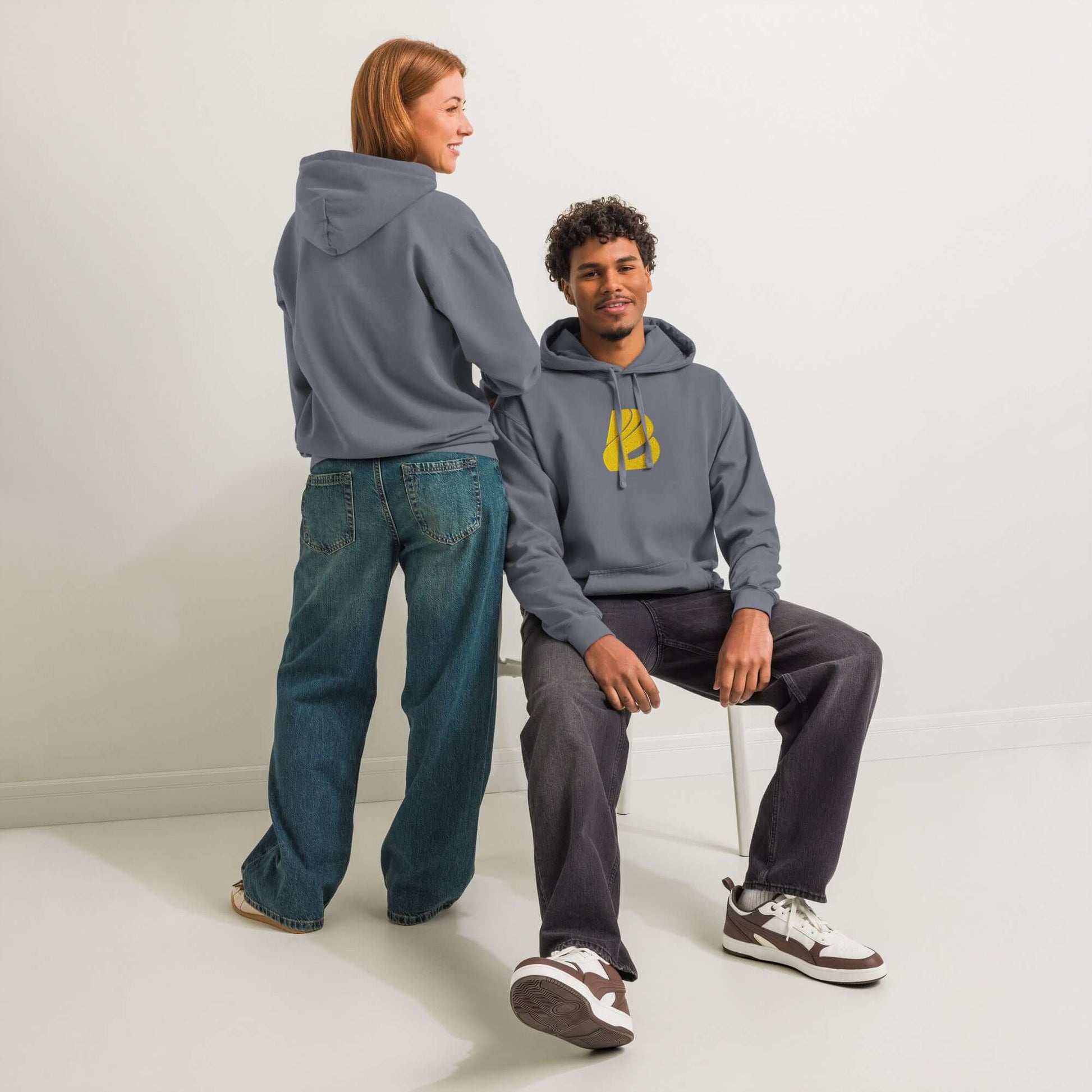 Two models wearing a Textilgefärbter Unisex-Hoodie with a relaxed fit and unique wash color in a studio setting.