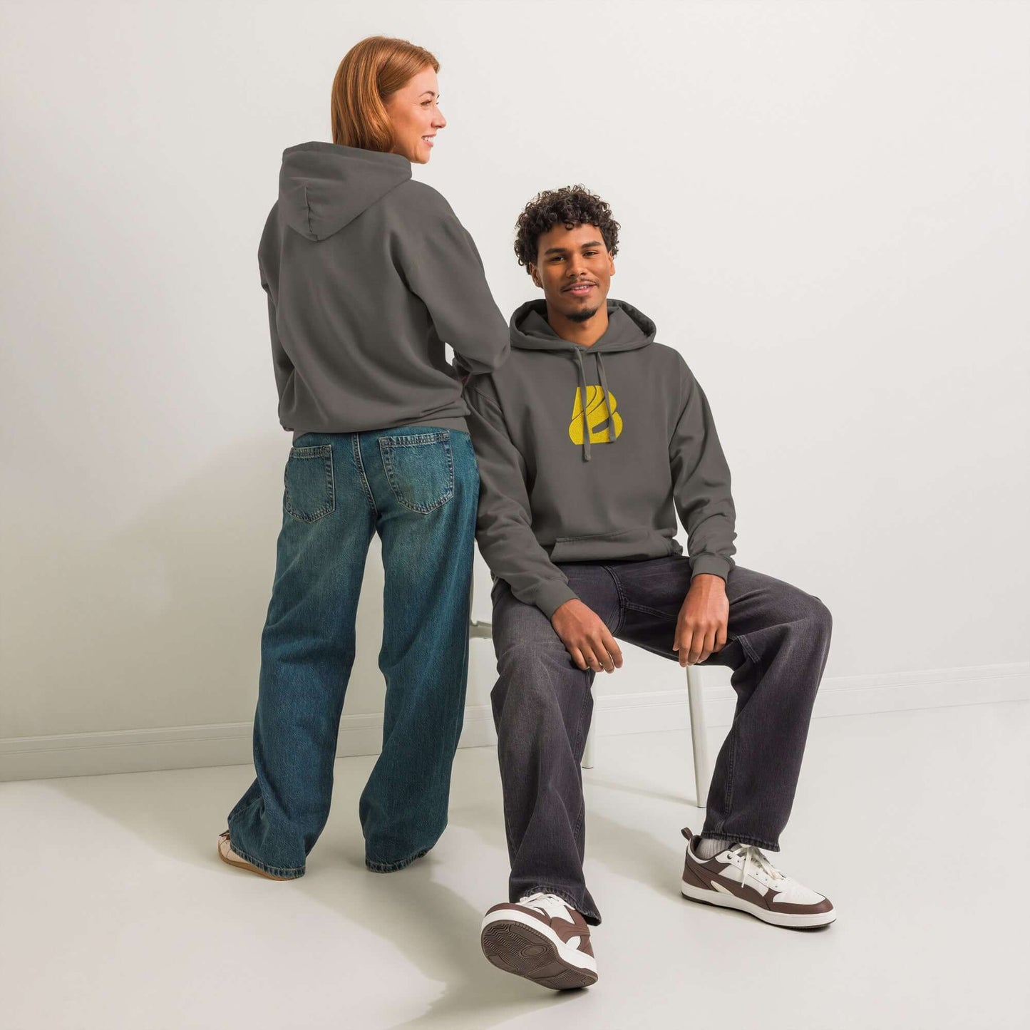 Zwei Modelle tragen einen textilgefärbten Unisex-Hoodie in entspannter Pose, zeigen Komfort und Stil in einem lässigen Setting.