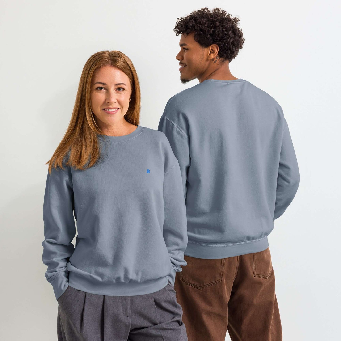 Zwei Personen tragen einen leichten textilgefärbten Unisex-Fleece-Pullover mit Rundhalsausschnitt in blauer Farbe, stilvoll casual gekleidet.