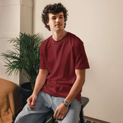 Man wearing Unisex-Bio-Baumwoll-T-Shirt in red, sitting indoors near a plant.
