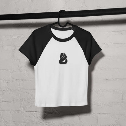 Kurz geschnittenes Feinripp-Raglan-T-Shirt für Damen in Weiß und Schwarz auf einem Kleiderbügel vor einer Ziegelwand.