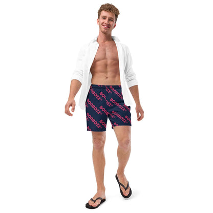 Man wearing Herren-Badehosen N°9, blue printed swim trunks, standing and smiling against a white background.