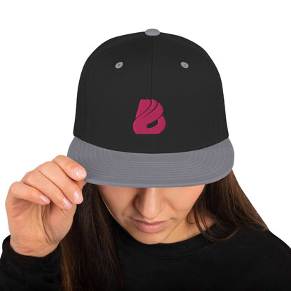 Person wearing Snapback-Cap N°3 with a black and grey design, featuring a red logo on the front, holding visor with hand.