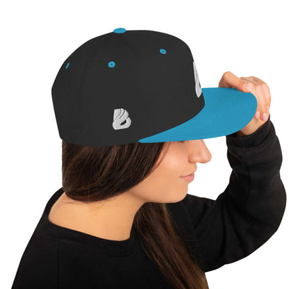 Woman wearing Snapback-Cap N°1 with blue brim and black top, featuring a structured 6-panel design and adjustable snap closure.