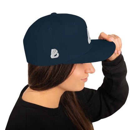 Woman wearing Snapback-Cap N°1 in navy blue with embroidered logo, featuring a flat brim and adjustable snap closure.