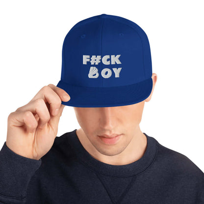 Person wearing a blue snapback cap with text "F#CK BOY" on the front, holding the visor with one hand.