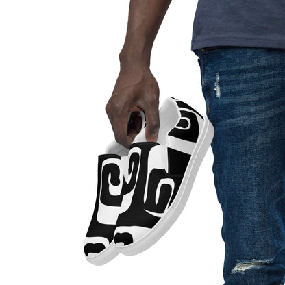 Herren-Canvas-Slipper N°0: Stylish black and white patterned men's slip-on shoes, lightweight with rubber soles, held by model in jeans.