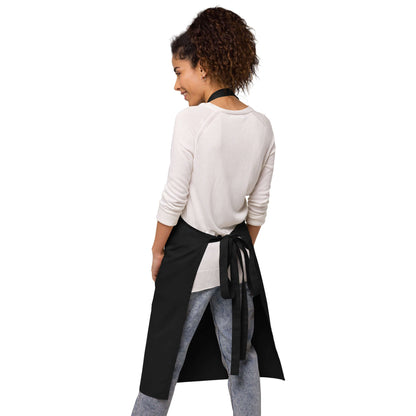 Woman wearing Schürze aus Bio-Baumwolle N°0, black apron, adjustable straps, front pockets. Perfect for kitchen protection and style.