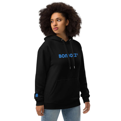 Woman wearing black "Bon Voiz" hoodie with blue text, showcasing a casual streetwear look. Hochwertiger Öko Kapuzenpullover N°7.