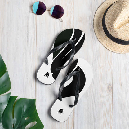 Alt Tag: Flip-Flops N°4 with bold black and white design on a beach setting with sunglasses, a hat, and tropical leaves for a summer vibe