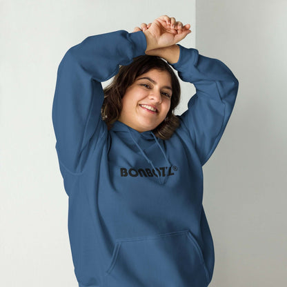 Woman wearing Unisex-Kapuzenpullover N°46 in blue, smiling and raising arms inside a room; cozy and stylish hoodie for cool evenings.