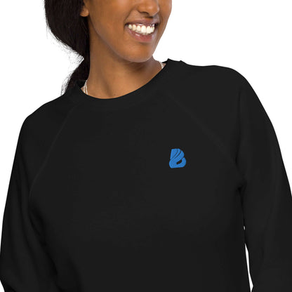 Woman wearing Unisex Bio-Raglan-Pullover N°1 in black with blue logo, featuring soft fleece lining and organic cotton exterior.