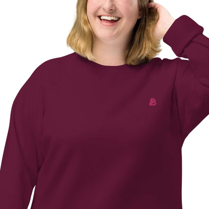 Woman wearing Unisex Bio-Raglan-Pullover N°2 in burgundy with minimalist logo, showcasing stylish comfort and organic cotton fabric.
