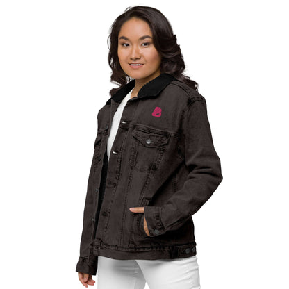 Woman wearing Unisex Sherpa Jeansjacke N°1 with black denim and pink logo, showcasing a warm Sherpa lining.